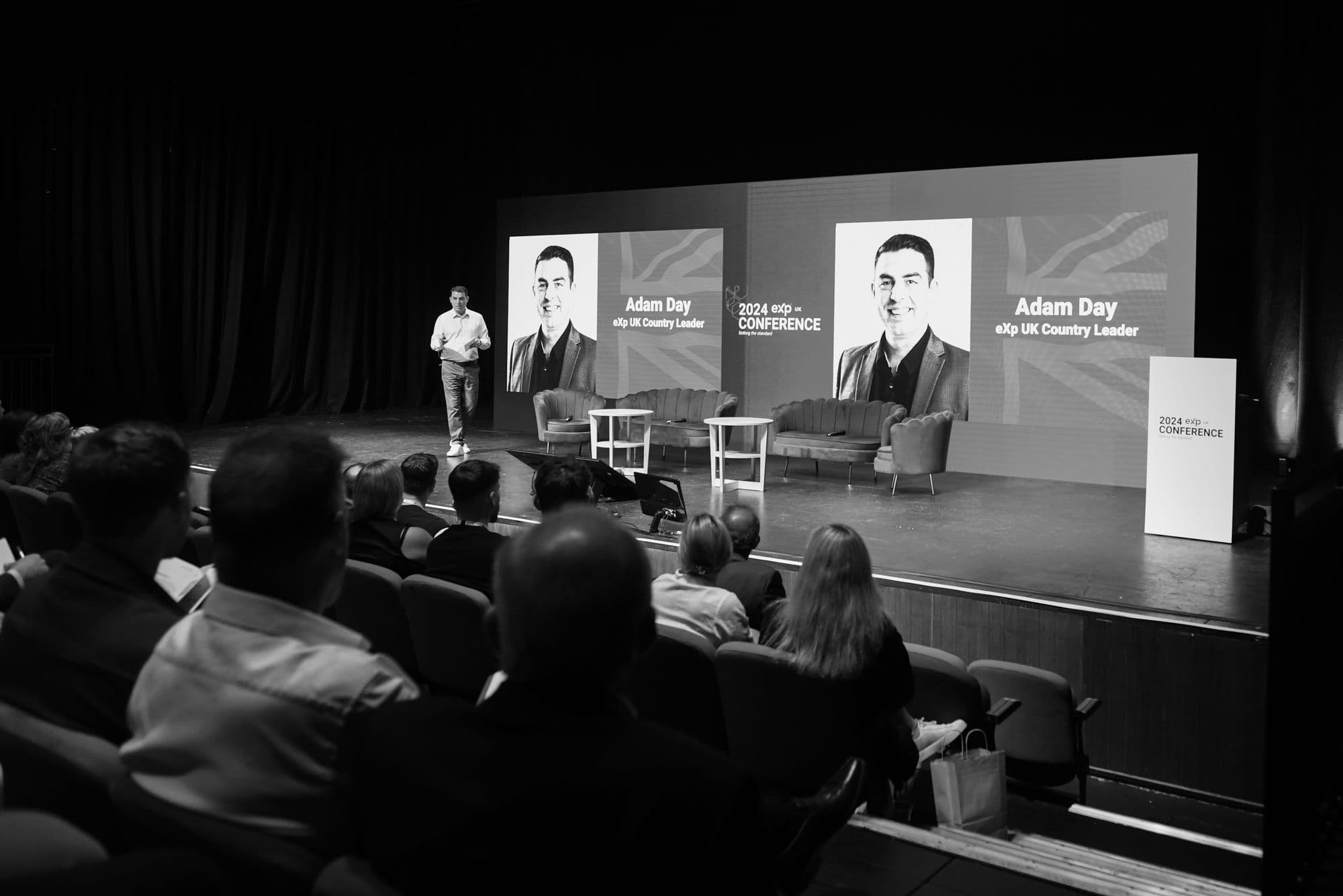 Adam Day on stage with name on screens — eXp UK Country Leader